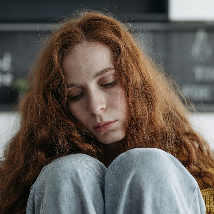 A young woman with red hair sits sadly on a couch.