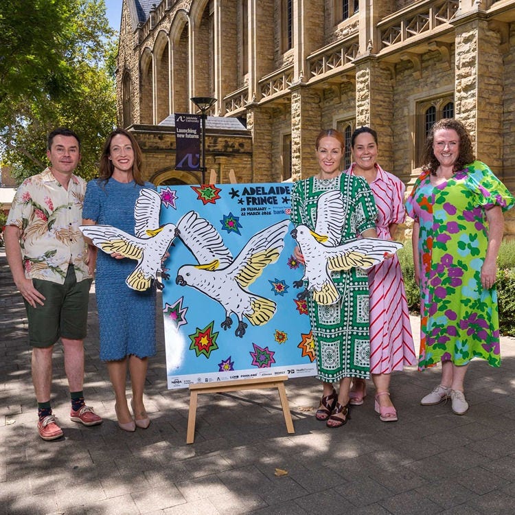 A group of five people stand by a brightly coloured sign.