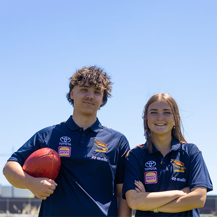 Two students in Adelaide Football Club tshirts smiling at the camera